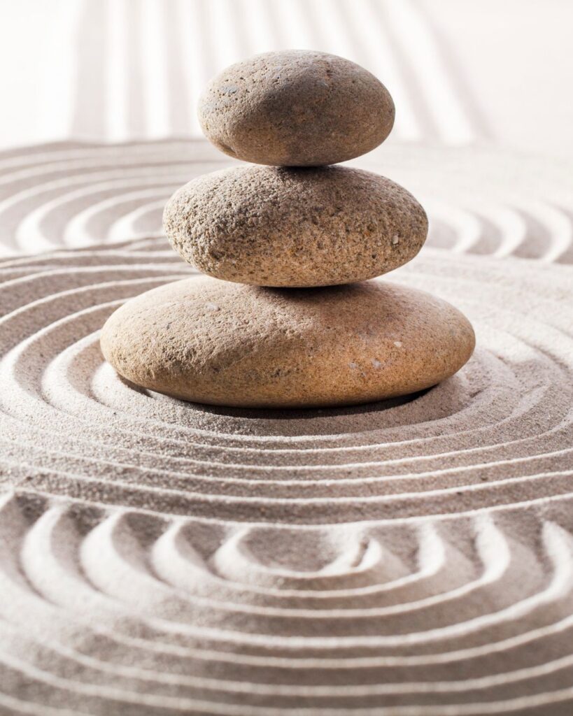 Drei runde Steine gestapelt im Zen-Garten mit konzentrischen Linien im Sand.